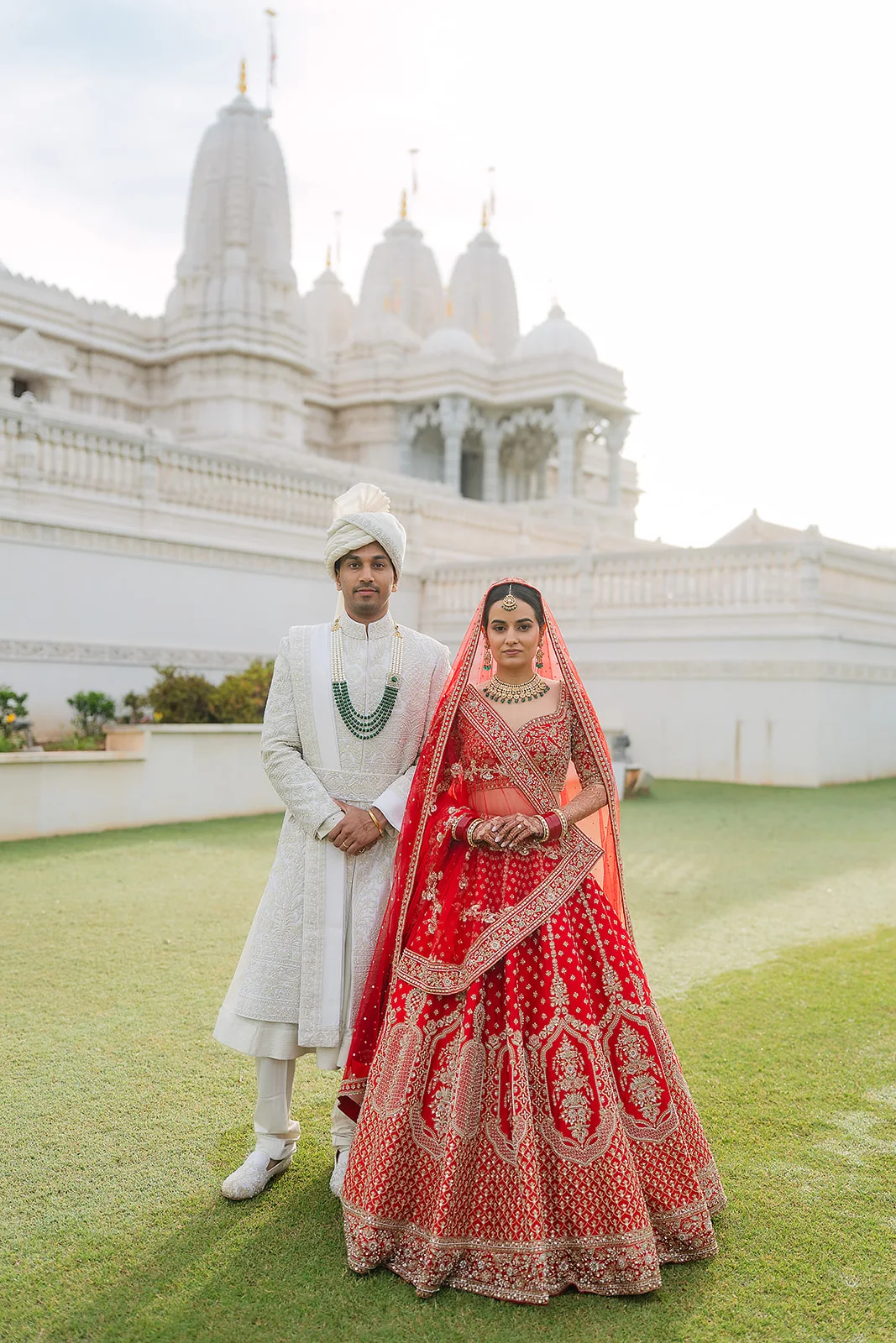 Couple in traditional wedding attire standing before a white temple